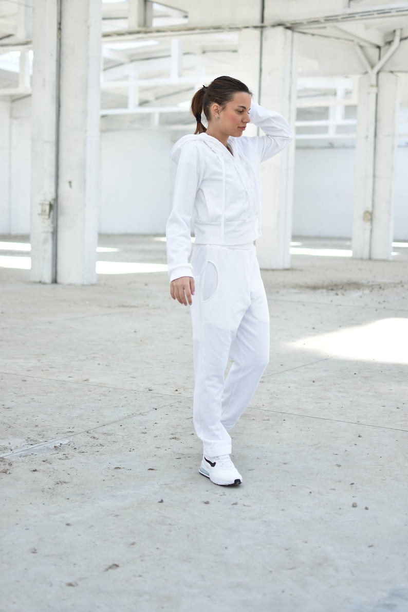 Puede incluir: Una sudadera con capucha blanca y un pantal&oacute;n de ch&aacute;ndal a juego con un solo bolsillo en la pierna izquierda. La modelo lleva zapatillas blancas.
