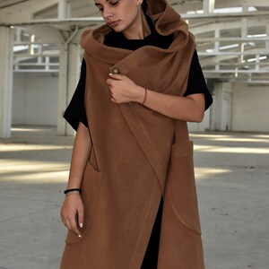 May include: A brown hooded wrap vest with a long, flowing design. The vest has a single button closure and two large pockets. The vest is made of a soft, comfortable fabric.