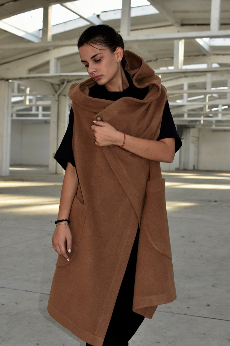 May include: A brown hooded wrap vest with a long, flowing design. The vest has a single button closure and two large pockets. The vest is made of a soft, comfortable fabric.