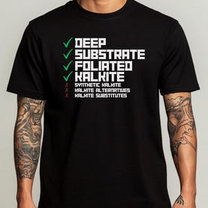 May include: Black t-shirt with white text and green check marks. The text reads "DEEP, SUBSTRATE, FOLIATED, KALKITE" with check marks, and "SYNTHETIC KALKITE, KALKITE ALTERNATIVES, KALKITE SUBSTITUTES" with X marks. The shirt is a crew neck.
