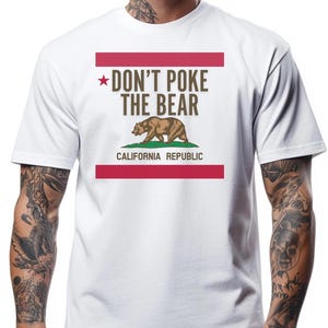 May include: White t-shirt with a graphic design. The design features the text "DON'T POKE THE BEAR" above a brown bear illustration, with the words "CALIFORNIA REPUBLIC" below. The design is framed by red bars.