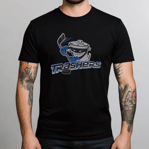 May include: Black t-shirt with a graphic of a trash can holding a hockey stick and the text "Trashers".