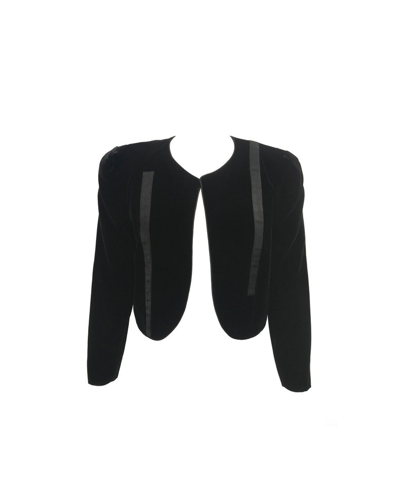 May include: A black velvet cropped jacket with a rounded neckline and long sleeves. The jacket has a fitted silhouette and features a satin trim along the edges.