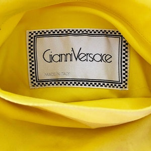 May include: A yellow fabric label with a black and white checkered border. The label reads "Gianni Versace" and "Made in Italy".