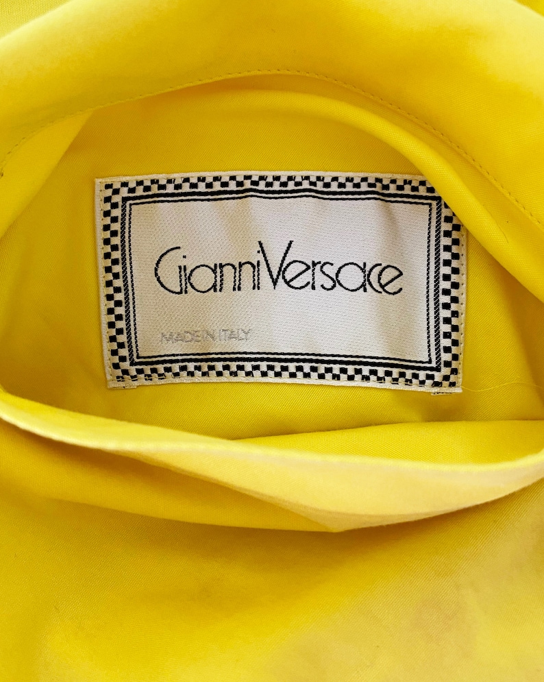 May include: A yellow fabric label with a black and white checkered border. The label reads "Gianni Versace" and "Made in Italy".