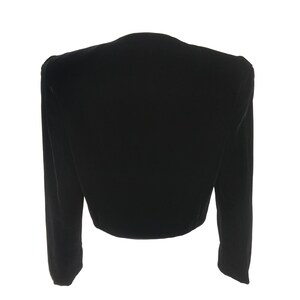 May include: A black velvet cropped jacket with long sleeves and a V-neck.