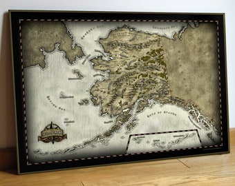 May include: Framed map of Alaska with a vintage aesthetic. The map features detailed illustrations of the state's terrain, waterways, and cities. The frame is black with a decorative stitched border. The map includes a compass rose emblem.