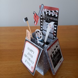 May include: A horror-themed pop-up birthday card. It features a chainsaw, a machete, and a film reel. The card includes the text "Happy 20th Birthday Jenny", "I'll be right back!", and "Dreamland".