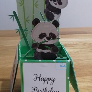 May include: A green pop-up card with a happy birthday message. The card features a 3D design of two pandas climbing bamboo.