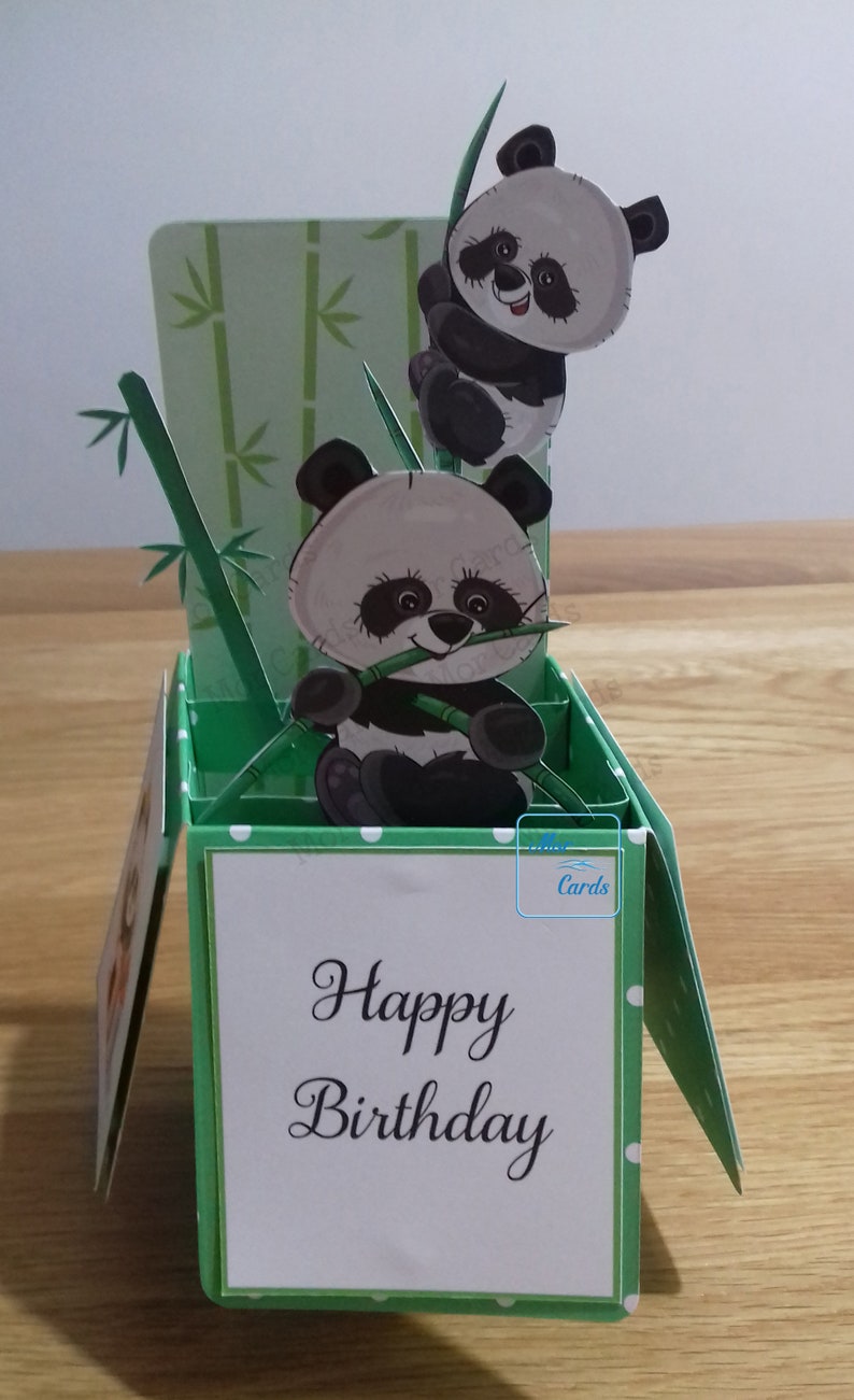 May include: A green pop-up card with a happy birthday message. The card features a 3D design of two pandas climbing bamboo.