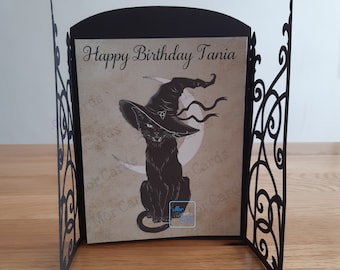 May include: A black card with a black cat wearing a witch's hat and a crescent moon behind it. The card says "Happy Birthday Tania".