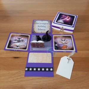 May include: A purple explosion box with a magical theme. The box has a bat, owl, and witch hat on the outside. The inside has a message that says "Have a magical birthday Rebecca".