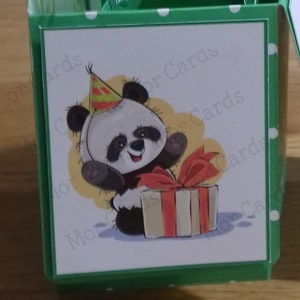 May include: A white card with a cartoon panda wearing a party hat and holding a gift box with a red ribbon. The card has a green border with white polka dots and the text "More Cards" in the bottom left corner.