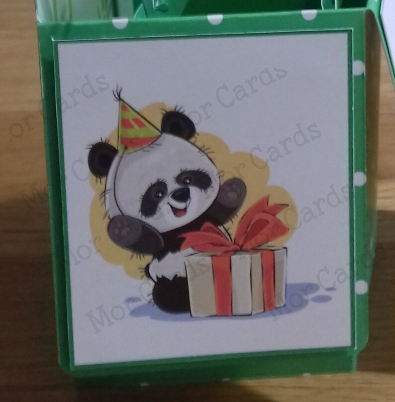 May include: A white card with a cartoon panda wearing a party hat and holding a gift box with a red ribbon. The card has a green border with white polka dots and the text "More Cards" in the bottom left corner.