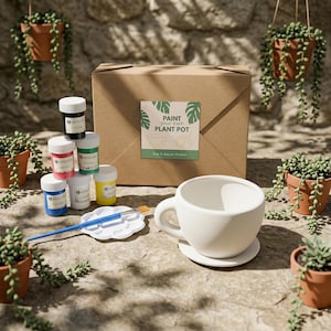 May include: A craft kit for painting a plant pot, featuring a large white ceramic cup with a saucer, paint pots in various colours, a paintbrush, and a cardboard box with the text "Paint Your Own Plant Pot."