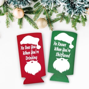 May include: Two Christmas-themed can coolers. One is red with the text "He Sees You When You're Drinking" and a white Santa silhouette. The other is green with the text "He Knows When You're Shitfaced" and a white Santa silhouette.