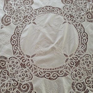 Peut inclure: Nappe en coton blanc avec une broderie de dentelle complexe en forme circulaire. La dentelle est délicate et détaillée, avec un motif floral.