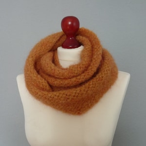 Könnte beinhalten: Ein warmer, orange-brauner gestrickter Infinity-Schal. Der Schal ist aus weichem, flauschigem Garn gefertigt und perfekt, um sich im Winter warm zu halten.
