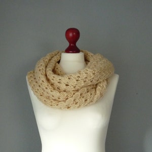 May include: A beige crocheted infinity scarf with a delicate openwork pattern. The scarf is displayed on a white mannequin.