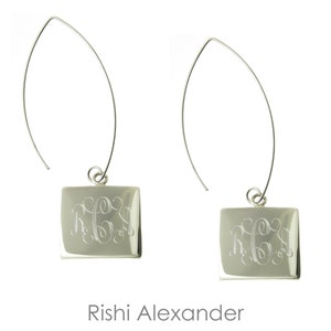 May include: Silver dangle earrings with a square charm featuring a monogrammed inscription. The earrings are made of silver and have a simple, elegant design.