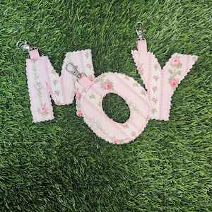 May include: Pink fabric letters spelling "MOM" with floral and striped patterns. Each letter has a silver key ring attached.
