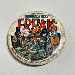 Może przedstawiać: Okrągły przypinany znaczek z kolorową ilustracją komiksową Fabulous Furry Freak Brothers. Tekst głosi "Fabulous Furry Freak Brothers", "There is a sucker born every minute" oraz "Produced by Real Free Press, Amsterdam, The Netherlands".
