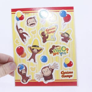 May include: A sheet of stickers featuring Curious George characters. The stickers are colorful and include images of Curious George, the Man with the Yellow Hat, and other characters from the show. The stickers also include the text "Curious George" and "Who? Are You?"