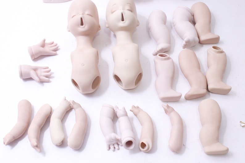 May include: A set of porcelain doll parts, including two heads, two torsos, six arms, and six legs. The parts are unpainted and ready to be customized.