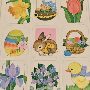 Puede incluir: Nueve pegatinas de Pascua coloridas que representan un narciso amarillo, un huevo de Pascua de chocolate, un tulipán rosa, un huevo de Pascua a rayas con una flor rosa, un conejito marrón con un lazo amarillo, una cesta de mimbre con huevos de Pascua coloridos, un iris morado, un ramo de flores moradas y azules y un patito amarillo con una cinta azul.