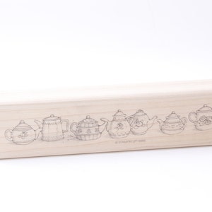 May include: A wooden stamp featuring a design of seven teapots arranged in a line. The teapots are all different shapes and sizes, with some featuring floral patterns. The text "© STAMPIN' UP! 1998" is at the bottom of the stamp.
