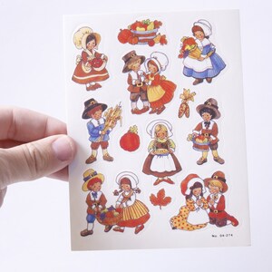 May include: A sheet of stickers featuring illustrations of children dressed in pilgrim clothing. The stickers depict various scenes of Thanksgiving, including children holding baskets of fruit, a cornucopia, and a pie. The stickers are printed on white paper with a light blue border. The text "No. 04-274" is printed in the bottom right corner.