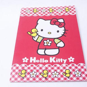 May include: A red Hello Kitty notepad featuring the iconic character holding a yellow bird. The notepad has a white and red gingham border with yellow chicks and white flowers. The words "Hello Kitty" are printed in white.