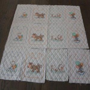 May include: Nine quilted fabric squares with embroidered images of a cow, a lamb, and a teddy bear holding balloons. Each square has a scalloped edge and is designed to be used as a bib.