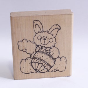 May include: A wooden stamp with a black and white illustration of a bunny holding an Easter egg.