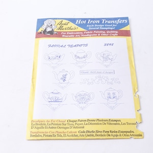 Può includere: Un foglio di trasferibili a caldo Aunt Martha's con disegni di teiere floreali. Il foglio presenta diverse illustrazioni di teiere blu, con il testo "FLORAL TEAPOTS" e "8898". Per ricamo, pittura su tessuto e altri lavori artigianali.