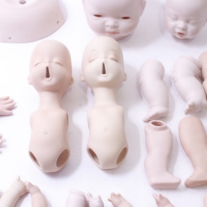 May include: A set of porcelain doll parts, including heads, torsos, legs, and arms. The parts are unpainted and ready to be customized.