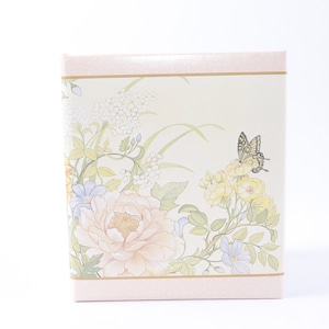 May include: A cream-colored box with a floral design featuring yellow, white, and blue flowers, green leaves, and a butterfly. The box has a pink border and a gold trim.
