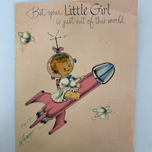 May include: Vintage greeting card with a pink background and the text "Bet your Little Girl is just out of this world." A cartoon baby in a space helmet rides a pink rocket ship, with planets in the background.