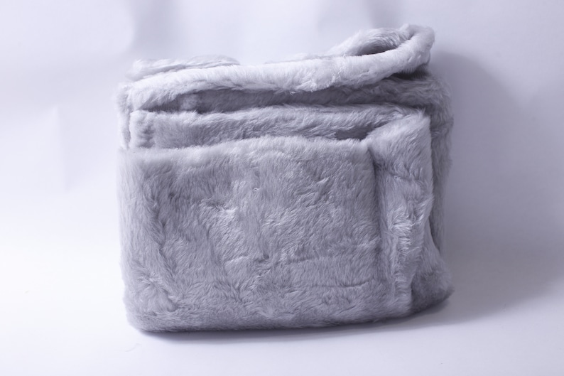 May include: A soft, gray plush blanket folded neatly. The blanket is made of a fuzzy, faux fur material.