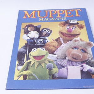 May include: A blue and yellow Muppet Magazine cover featuring Kermit the Frog, Miss Piggy, Fozzie Bear, and Gonzo the Great. The magazine cover has the text "Muppet Magazine" and "Press" on a hat.