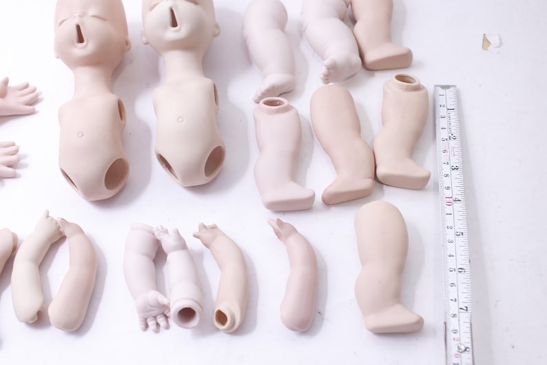 May include: A set of porcelain doll parts, including two heads, two torsos, six arms, and four legs. The parts are unpainted and ready to be customized.
