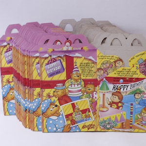 May include: A collection of vintage Happy Meal boxes, each with a pink top and yellow sides. The boxes are decorated with illustrations of The Berenstain Bears and Cabbage Patch Kids, and the text "Happy Birthday Happy Meal".