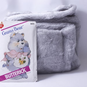 May include: A vintage Care Bears sewing pattern featuring Grams Bear, a blue bear with a pink ribbon and a yellow rose. The pattern is from Butterick and has the number 6933.