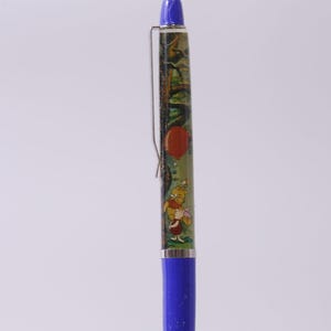 Op de afbeelding: Een blauwe pen met een decoratieve schacht met een cartoonillustratie van Winnie de Poeh, een rode ballon en een bosscène. De pen heeft een zilveren clip en een blauwe punt.