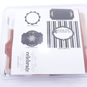 May include: A set of six clear rubber stamps with black ink. The stamps feature various designs, including a circle, a label with the text "winter wishes", a label with the text "from the kitchen of", a striped pattern, and the word "celebrate".