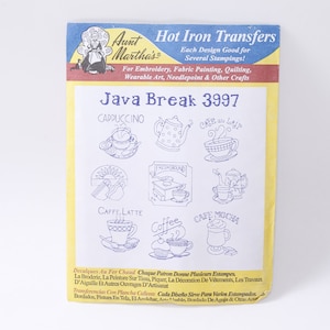 Op de afbeelding: Een geel en blauw pakket met strijktransfers voor knutselen. Het pakket bevat verschillende ontwerpen van koffiekopjes met namen als "Cappuccino", "Caffe Latte" en "Cafe Mocha". Het pakket is getiteld "Java Break 3997" en is van Aunt Martha's.