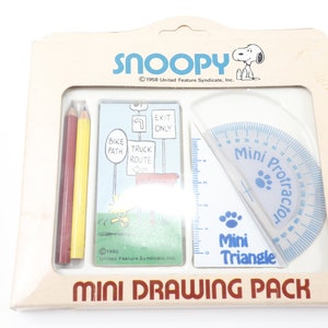 May include: A white cardboard box with a drawing set featuring a Snoopy illustration. The set includes two colored pencils, a mini protractor, a mini triangle, and a card with a Snoopy illustration. The box has the text "Snoopy" and "Mini Drawing Pack" printed on it.