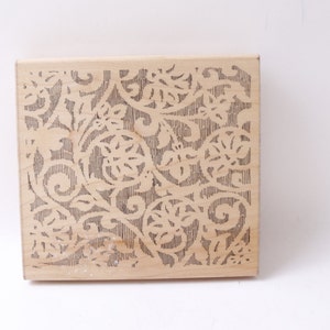 May include: A wooden stamp featuring a decorative floral design. The design is carved into the wood and is a light brown colour.