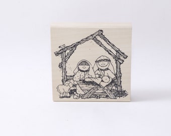 May include: A black and white illustration of a nativity scene with Mary, Joseph, and baby Jesus in a manger. A sheep is standing to the left of the manger.