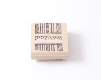 Könnte beinhalten: Ein Stempel aus Holz mit einem geometrischen Muster in Schwarzweiß. Das Muster zeigt Streifen und Punkte.